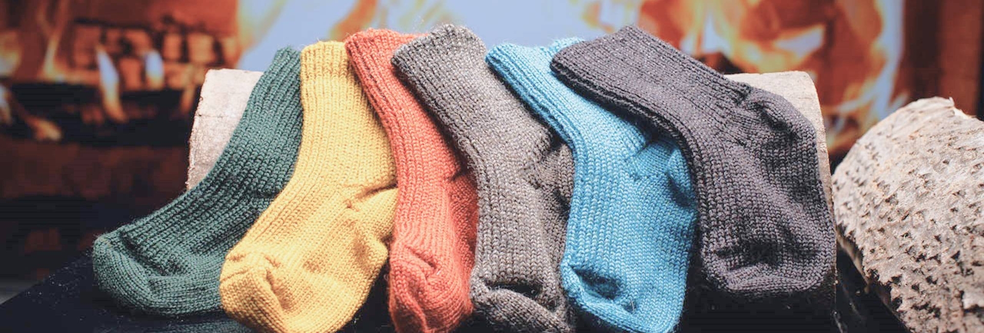 Bunte, gestrickte Socken liegen vor einem Kamin. Gemütliche, warme Atmosphäre