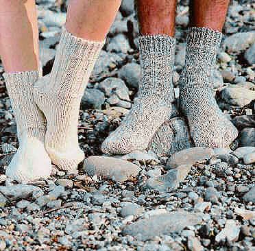 Ein Paar Personen trägt handgestrickte Socken, die auf einem steinigen Untergrund stehen