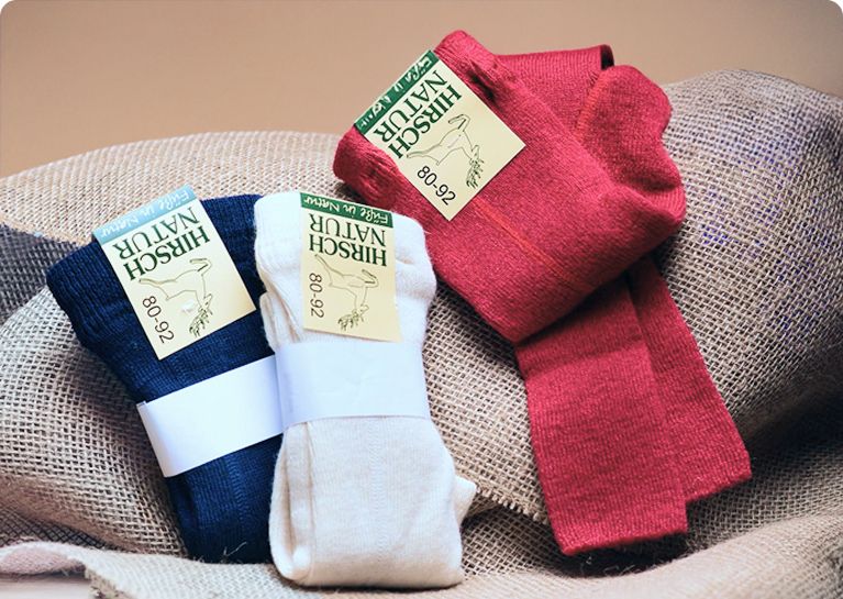 Drei zusammengefaltete Hirsch Natur Strumpfhosen in Dunkelblau, Hellbeige und Rot auf einem Jutesack